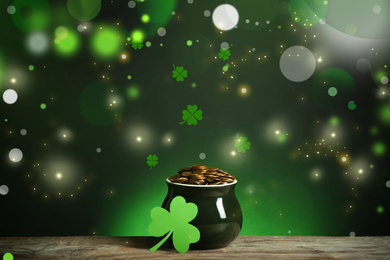 Pot with gold coins and clover on wooden table against dark background. St. Patrick's Day