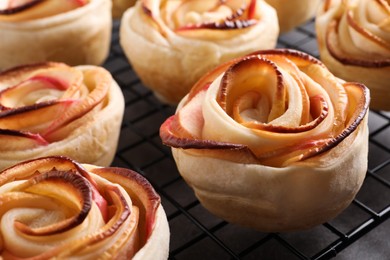 Photo of Cooling rack with freshly baked apple roses on grey table, closeup. Beautiful dessert