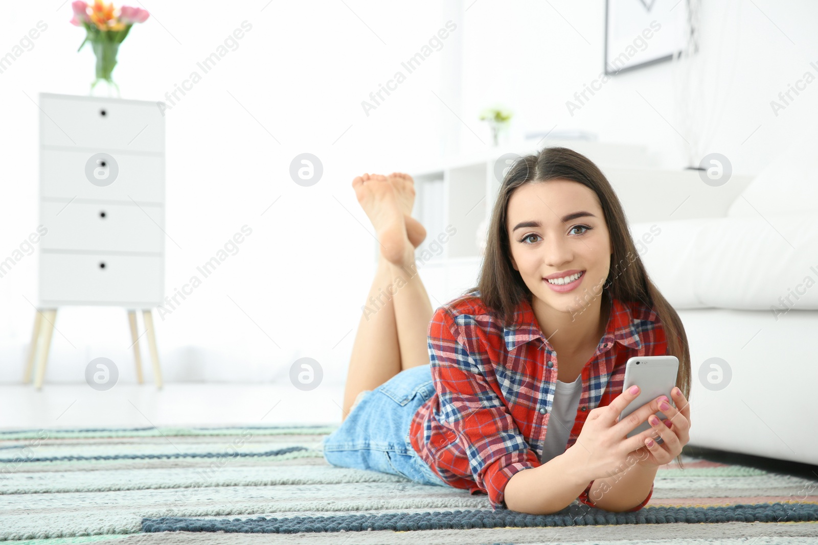 Photo of Attractive young woman using mobile phone on floor at home