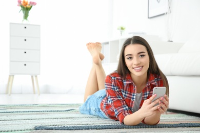 Photo of Attractive young woman using mobile phone on floor at home