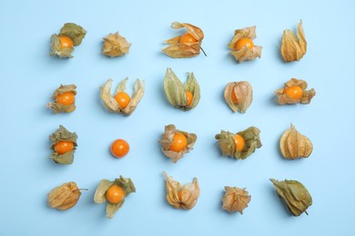Ripe physalis fruits with dry husk on light blue background, flat lay