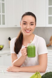 Beautiful young woman holding mason jar with delicious smoothie in kitchen