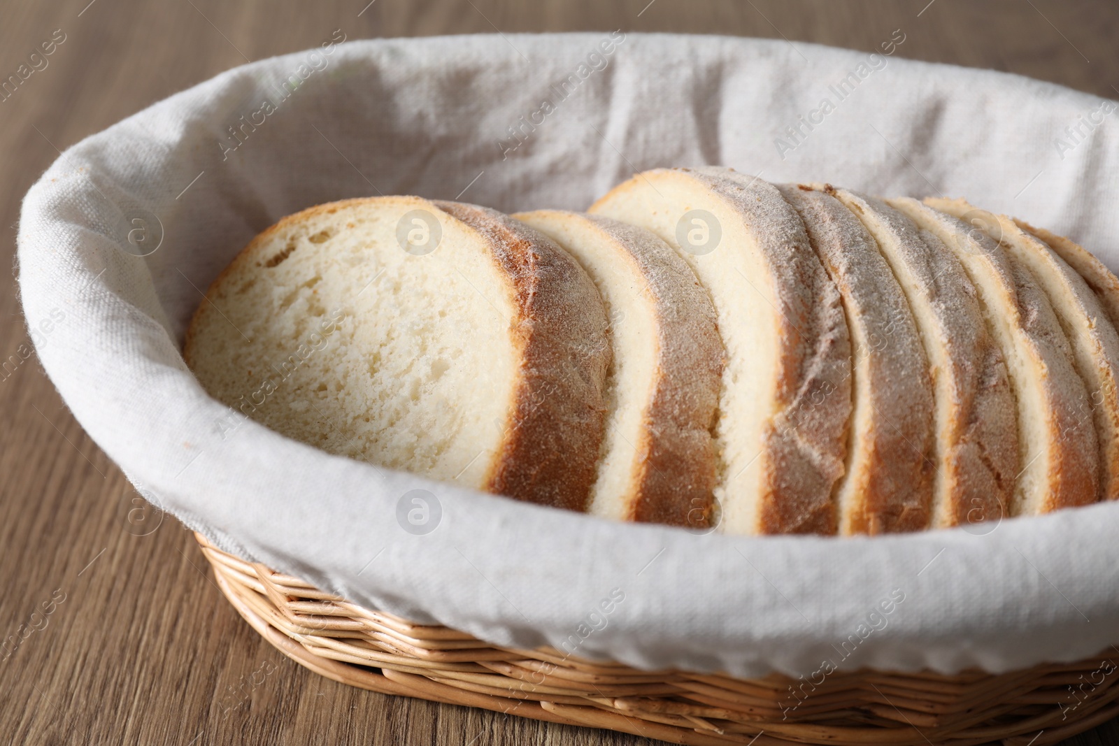 Photo of Fresh bread slices in wicker basket on wooden table, closeup