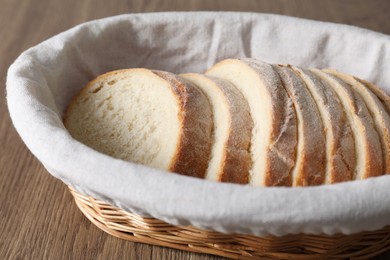 Fresh bread slices in wicker basket on wooden table, closeup