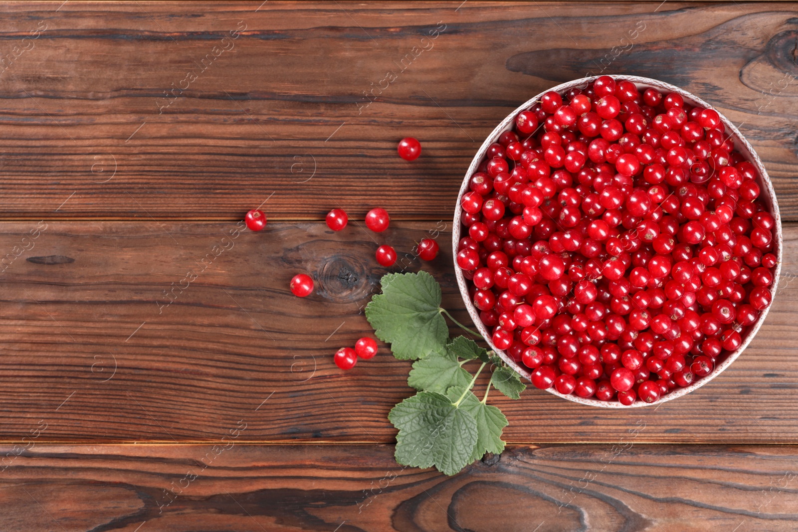 Photo of Ripe red currants and leaves on wooden table, flat lay. Space for text