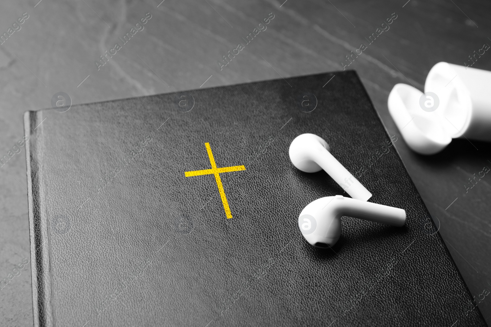 Photo of Bible and earphones on black table, closeup. Religious audiobook