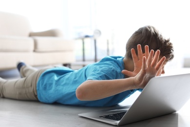 Photo of Frightened little child with laptop on floor indoors. Danger of internet