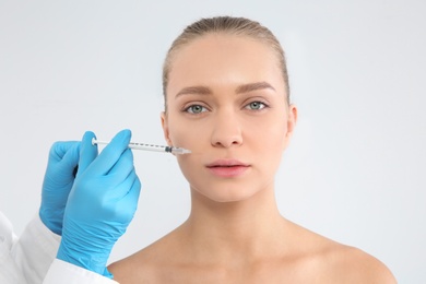 Photo of Young woman getting facial injection on white background. Cosmetic surgery concept