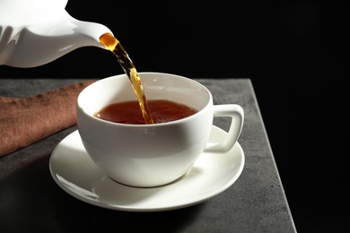 Pouring hot tea into white porcelain cup on dark table