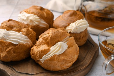 Delicious profiteroles filled with cream on white tiled table, closeup