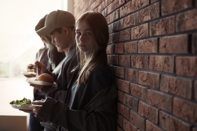 Photo of Teenage girl and other poor people with food at brick wall indoors. Space for text