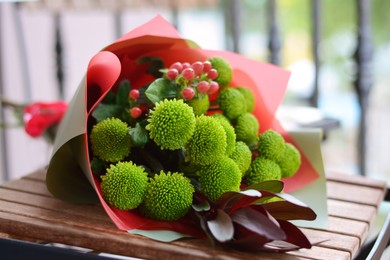 Photo of Bouquet of beautiful flowers wrapped in paper on wooden table, closeup