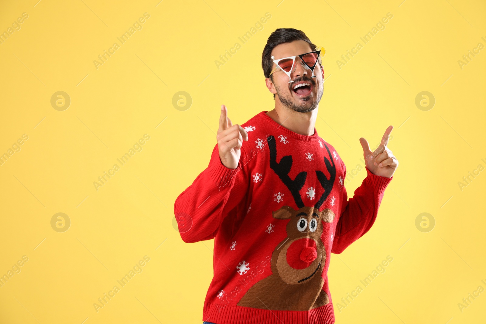 Photo of Happy man in Christmas sweater and party glasses on yellow background