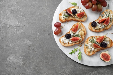 Photo of Bruschettas with cheese, figs and blackberries served on grey table, top view. Space for text