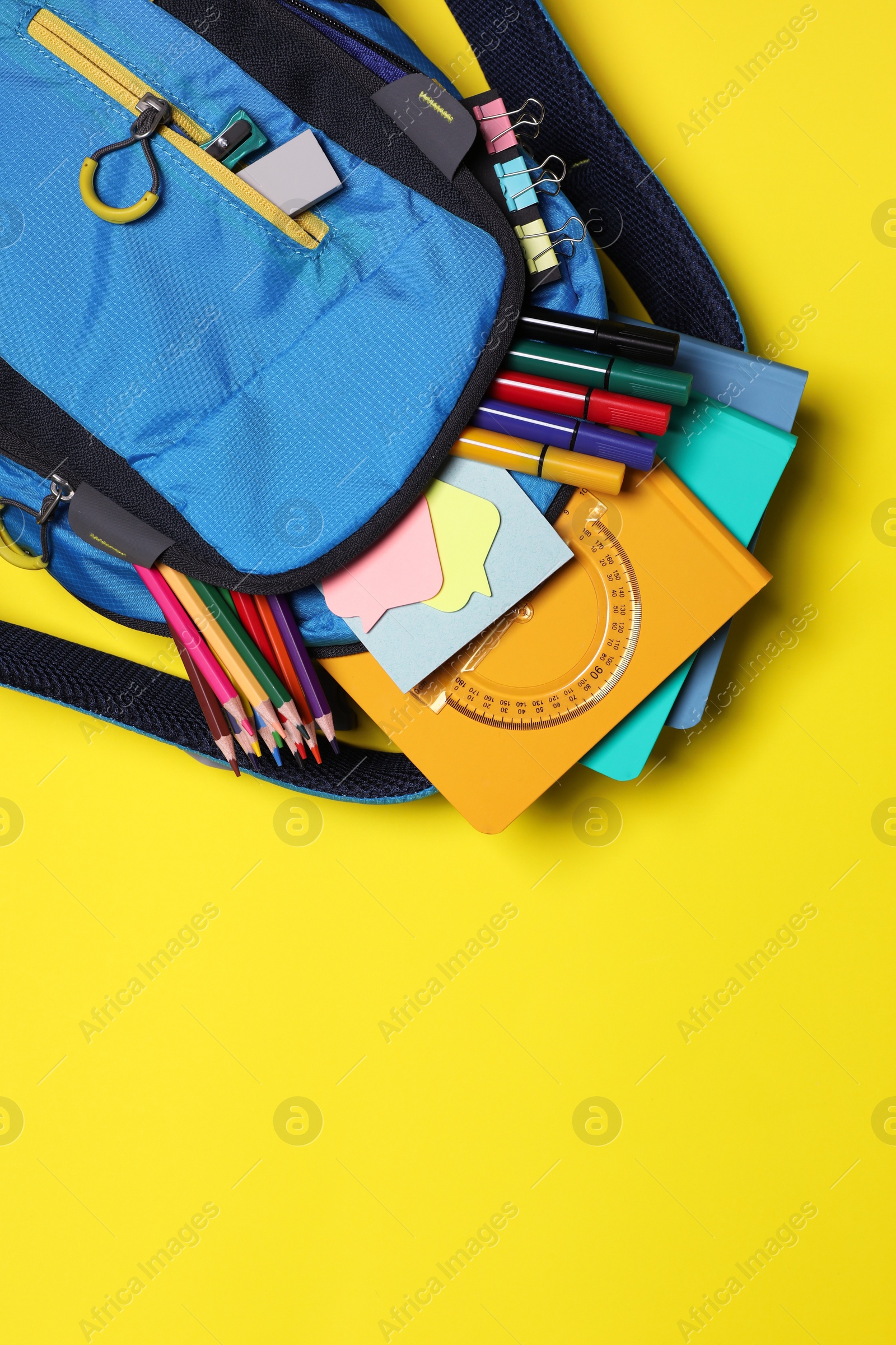 Photo of Backpack with school stationery on yellow background, top view. Space for text