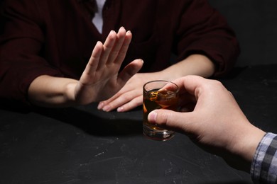 Photo of Alcohol addiction. Woman refusing glass of whiskey at dark table, closeup