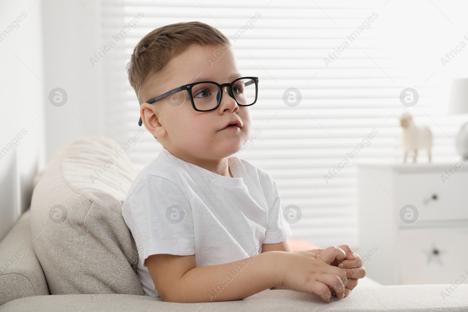 Photo of Cute little boy in glasses on sofa at home. Space for text