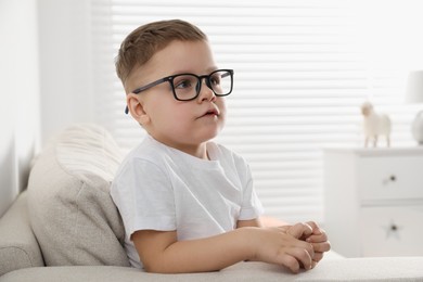 Cute little boy in glasses on sofa at home. Space for text