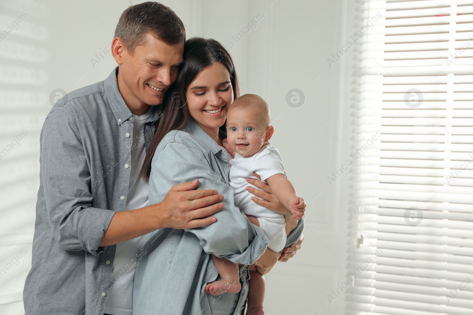 Photo of Happy family. Couple with their cute baby near window indoors, space for text