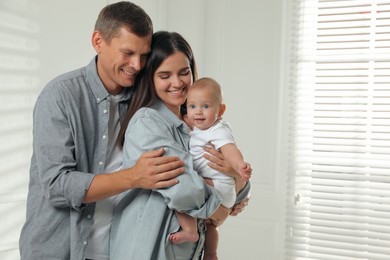 Happy family. Couple with their cute baby near window indoors, space for text