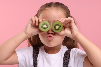 Photo of Girl covering eyes with halves of fresh kiwi on pink background