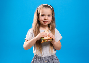 Cute little girl with tasty sandwich on light blue background