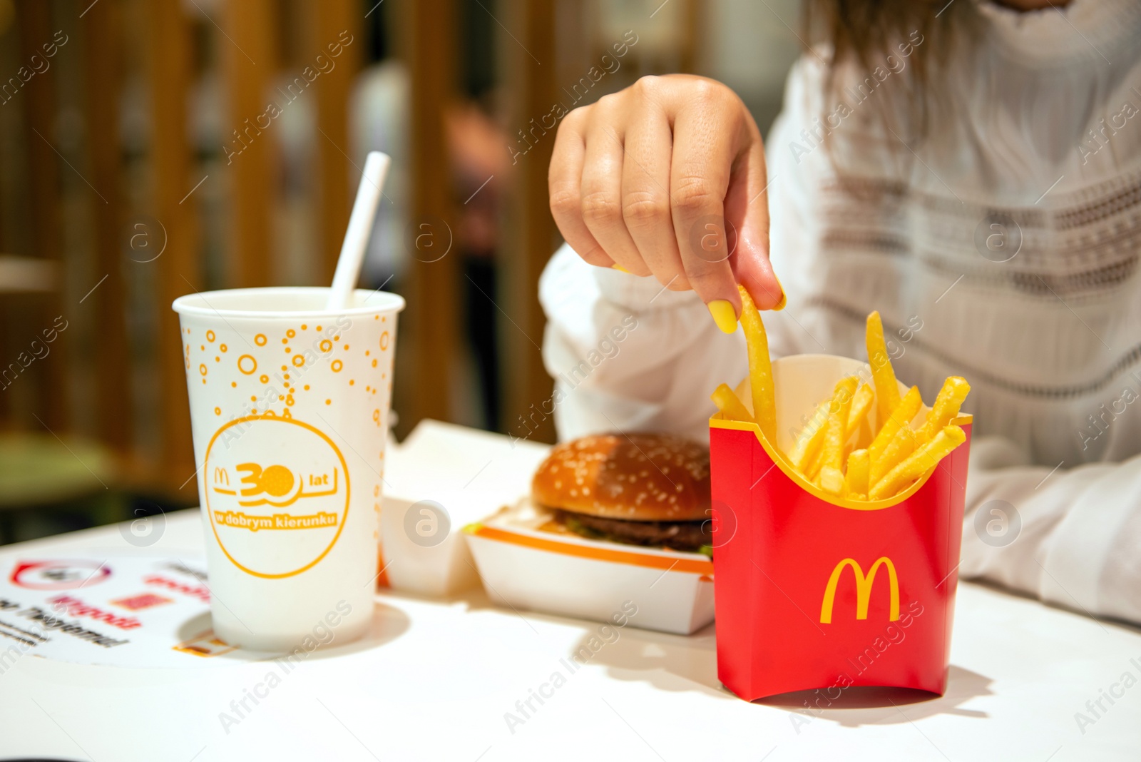 Photo of WARSAW, POLAND - SEPTEMBER 04, 2022: Woman with McDonald's French fries, burger and drink at table in cafe, closeup