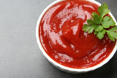 Photo of Delicious tomato ketchup and parsley in bowl on grey textured table, closeup. Space for text