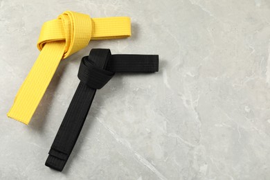 Photo of Black and yellow karate belts on gray marble background, flat lay. Space for text