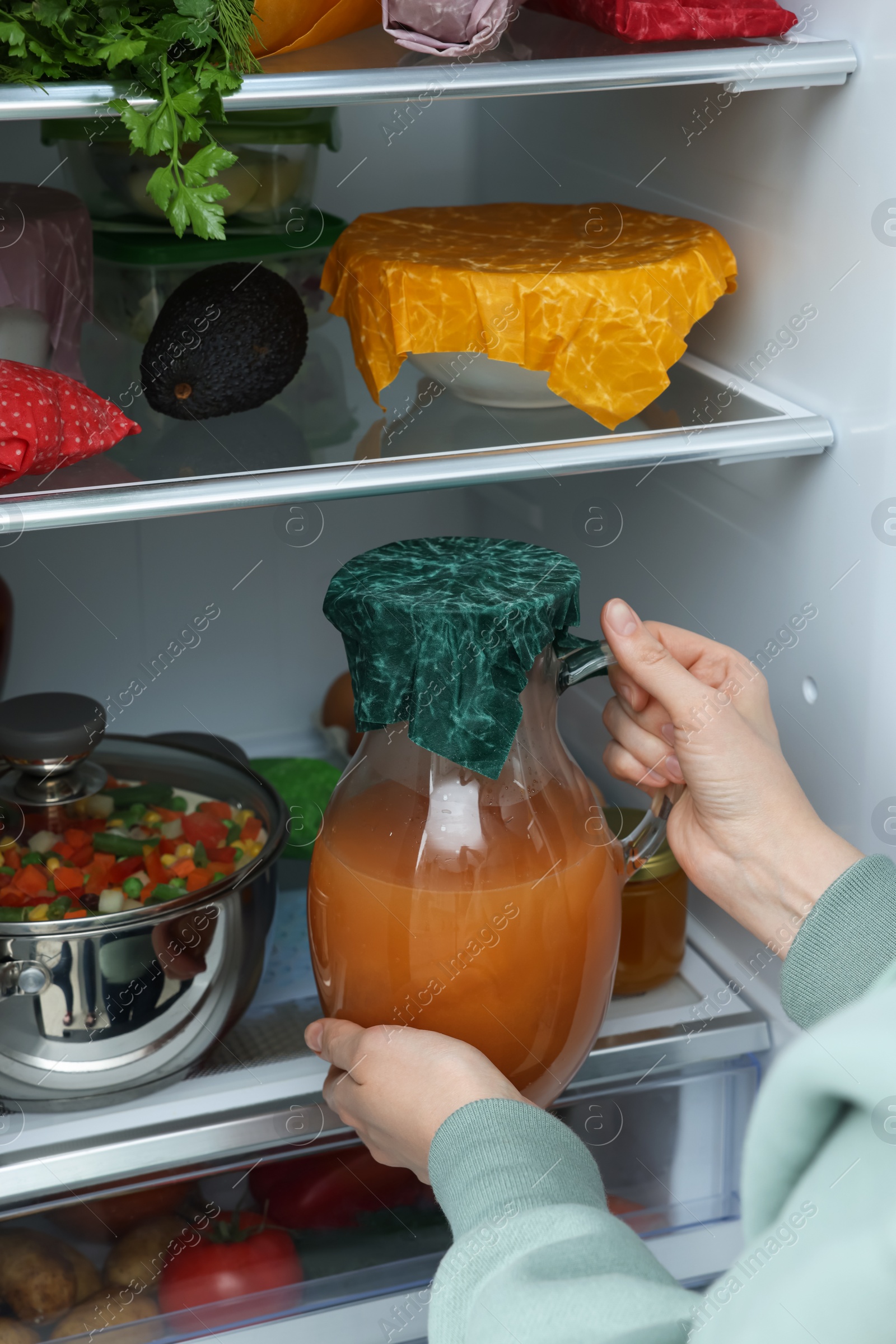 Photo of Woman taking jug covered with beeswax food wrap from refrigerator, closeup