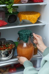 Photo of Woman taking jug covered with beeswax food wrap from refrigerator, closeup