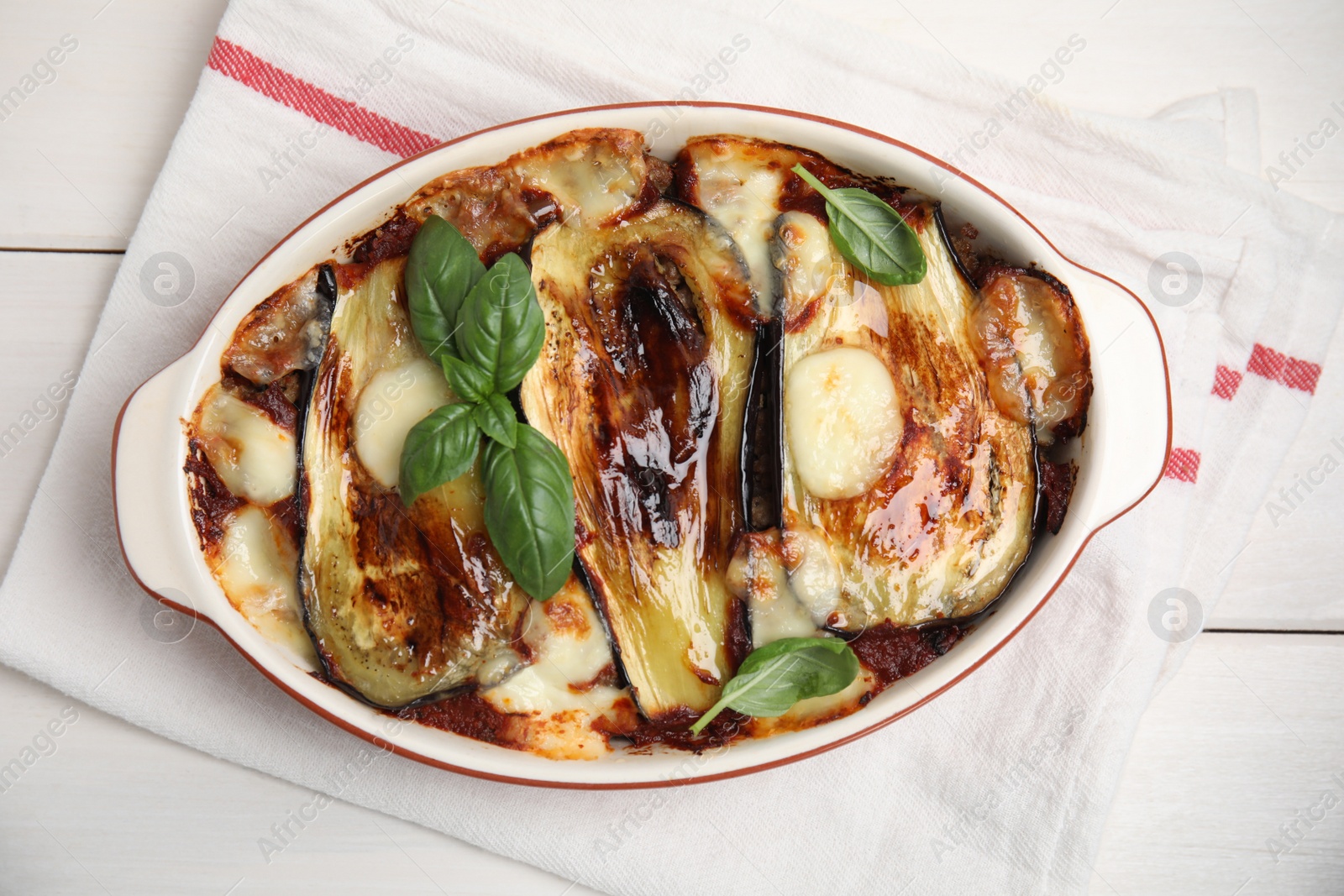 Photo of Delicious eggplant lasagna in baking dish and napkin on white wooden table, top view