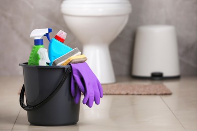 Bucket with cleaning supplies on floor in bathroom, space for text