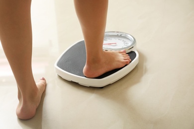 Photo of Woman stepping on floor scales indoors. Overweight problem