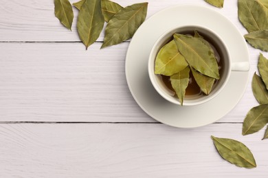 Cup of freshly brewed tea with bay leaves on white wooden table, flat lay. Space for text