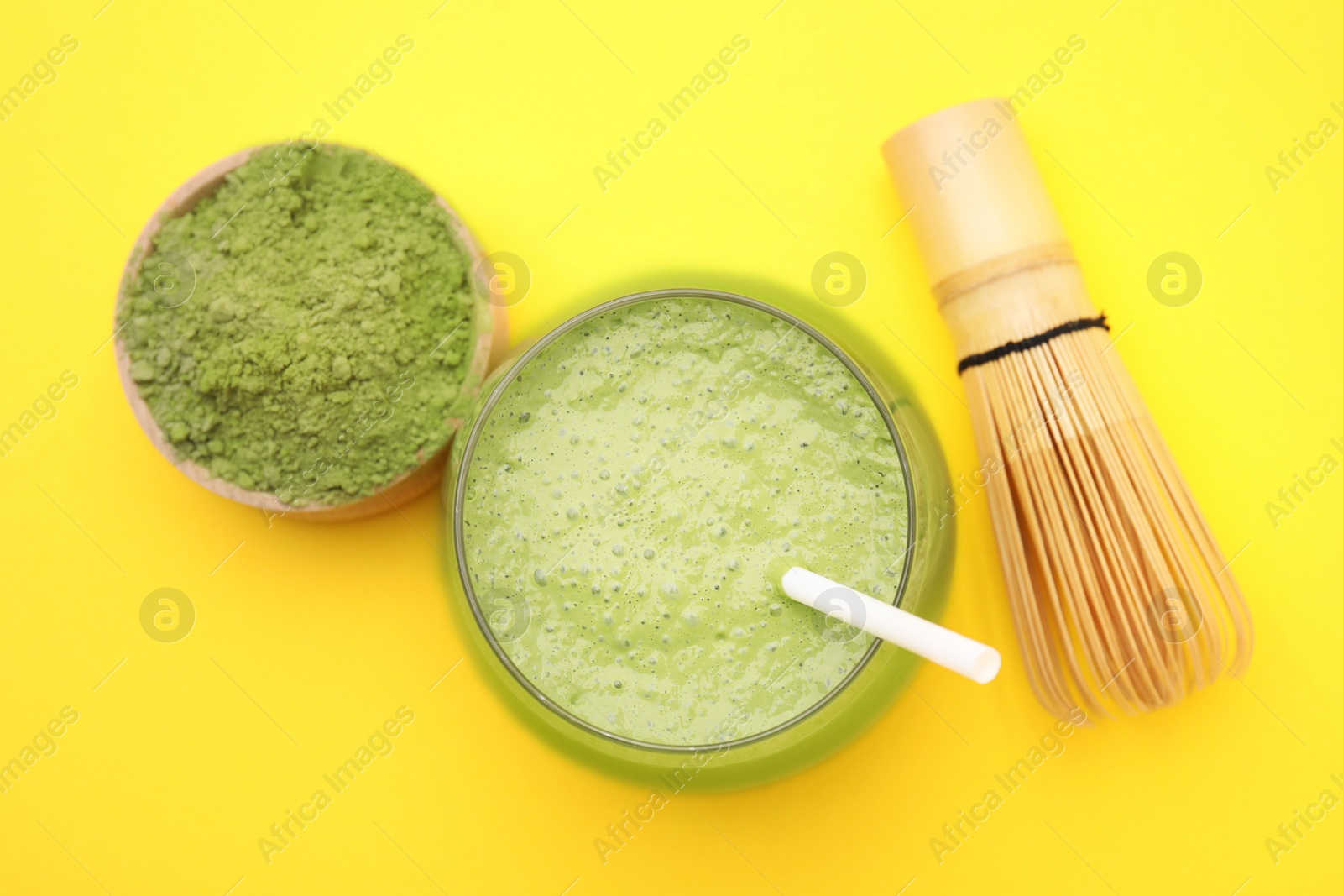 Photo of Glass of tasty matcha smoothie, powder and bamboo whisk on yellow background, flat lay