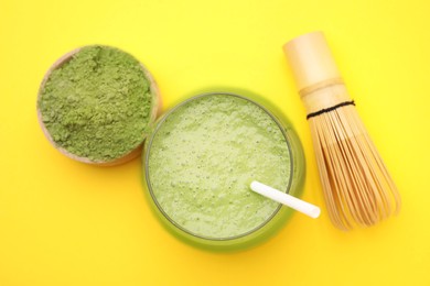 Glass of tasty matcha smoothie, powder and bamboo whisk on yellow background, flat lay