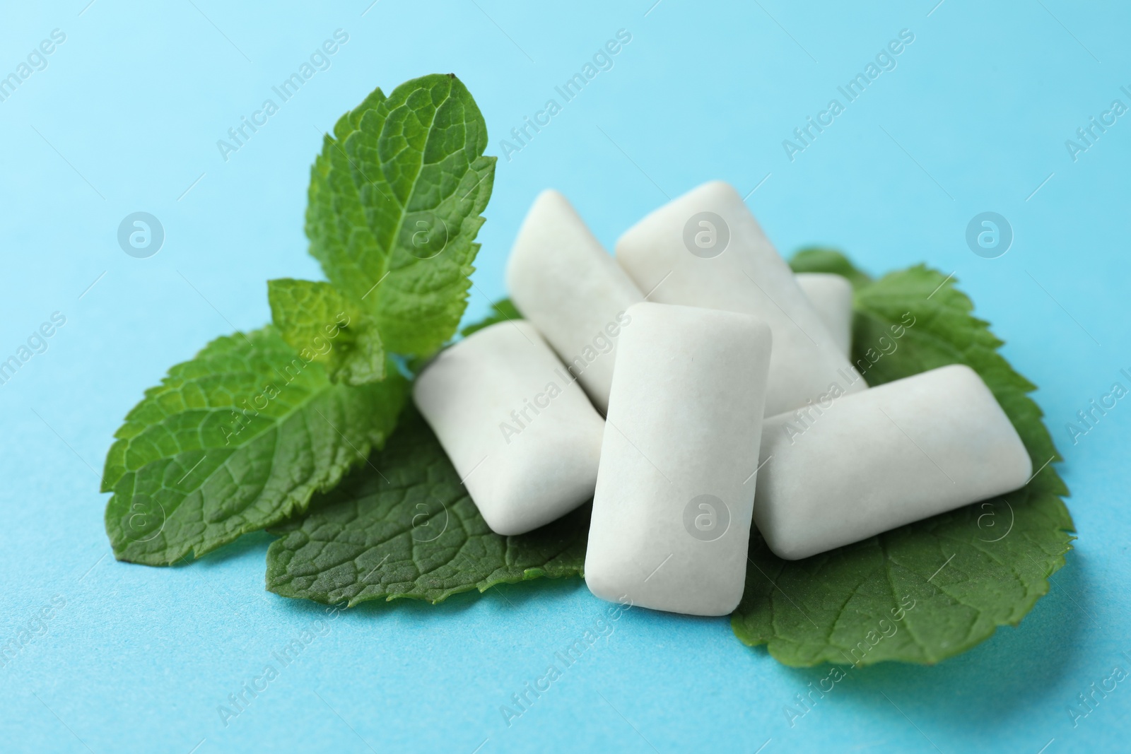 Photo of Tasty white chewing gums and mint leaves on light blue background, closeup