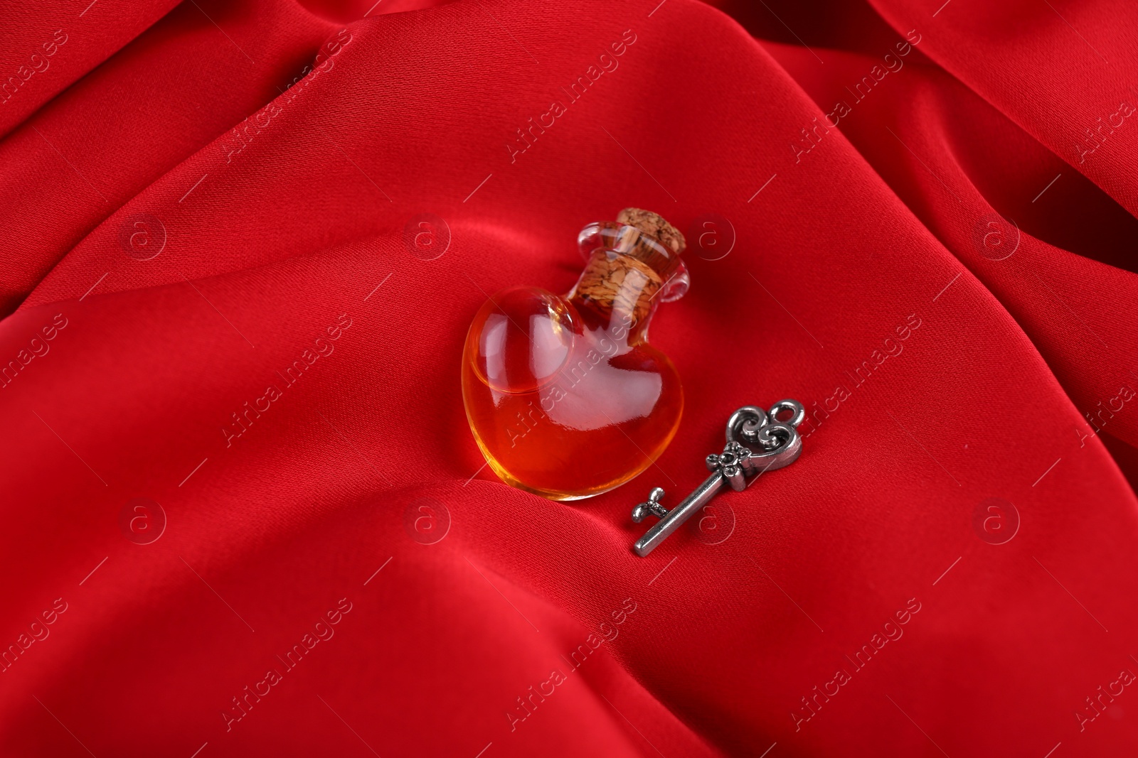 Photo of Heart shaped bottle of love potion with small key on red fabric