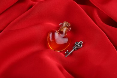 Photo of Heart shaped bottle of love potion with small key on red fabric