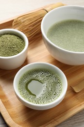 Photo of Fresh matcha tea, bamboo whisk and green powder on wooden tray, closeup