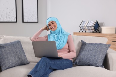 Photo of Muslim woman using laptop at couch in room
