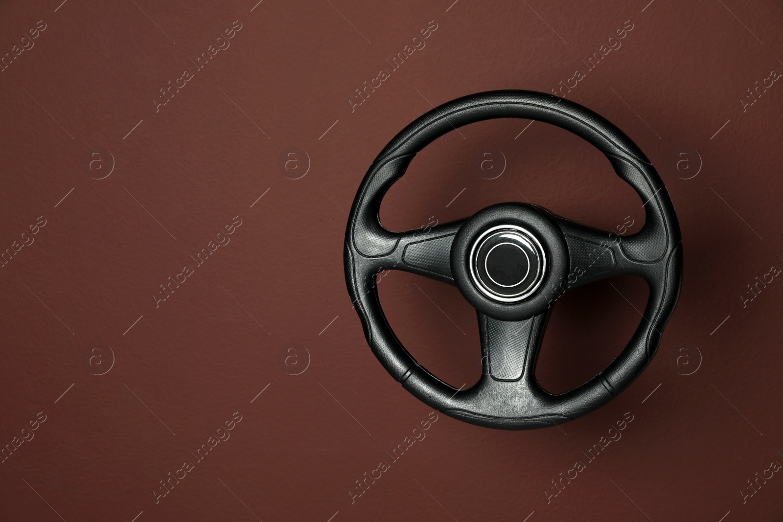 Photo of New black steering wheel on brown background, space for text