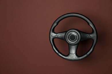 Photo of New black steering wheel on brown background, space for text