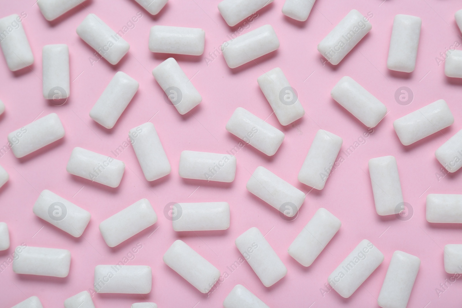 Photo of Tasty white chewing gums on pale pink background, flat lay