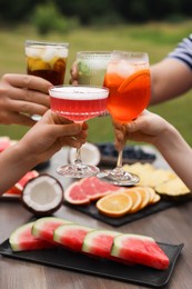 Photo of Friends clinking glasses with cocktails at table outdoors, closeup