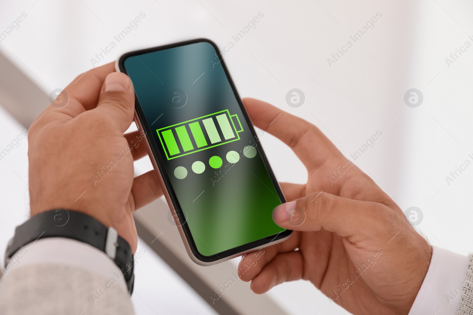 Image of Young man holding smartphone with fully charged battery indoors, closeup