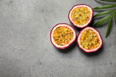 Halves of passion fruits (maracuyas) and palm leaf on grey table, flat lay. Space for text