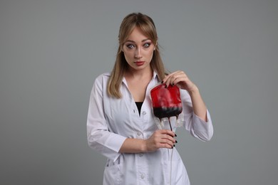 Photo of Woman in scary nurse costume with blood bag on light grey background. Halloween celebration