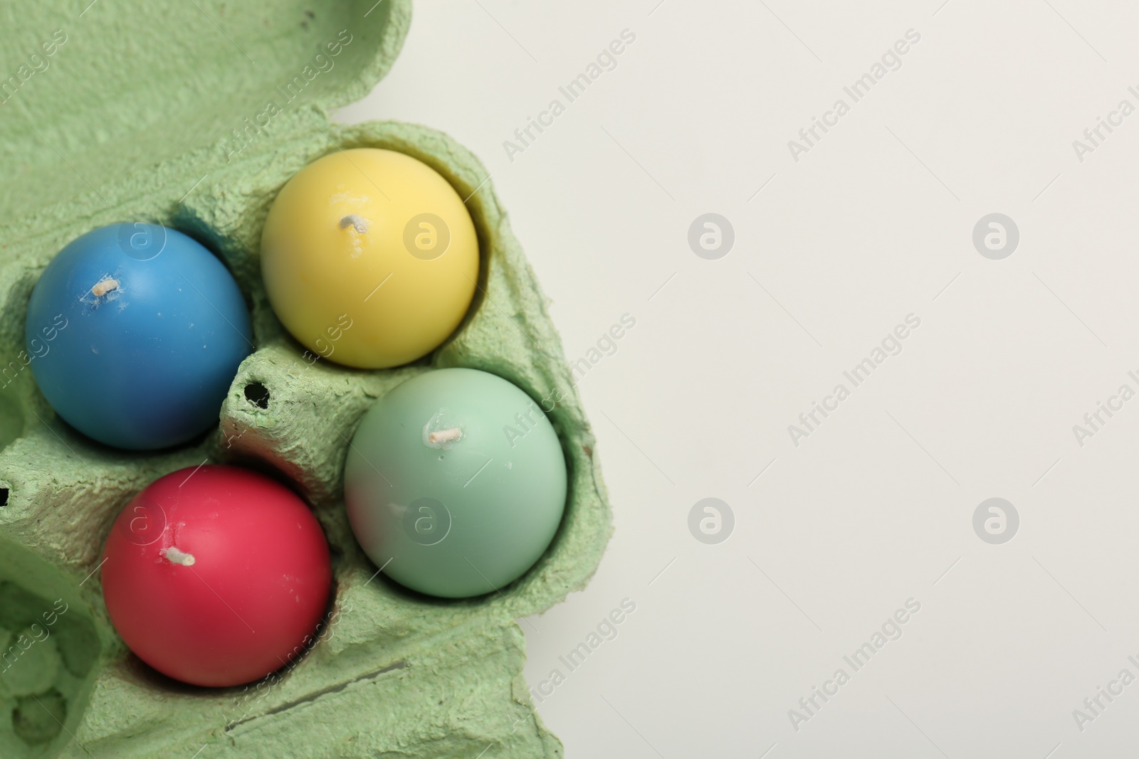 Photo of Colorful egg shaped candles in carton on white table, top view. Easter decor